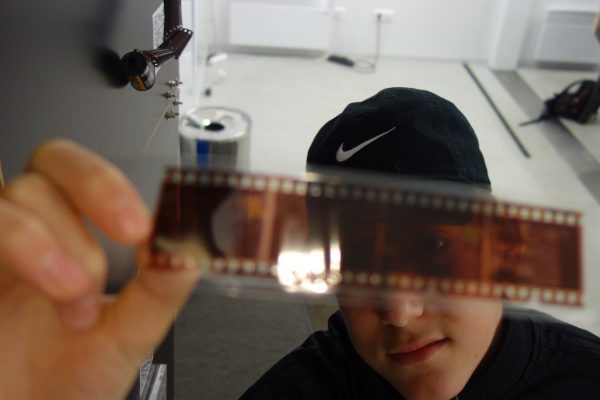 Ein Bursche betrachtet die Negative auf einem analogen Filmstreifen, den er gegen das Licht hält.