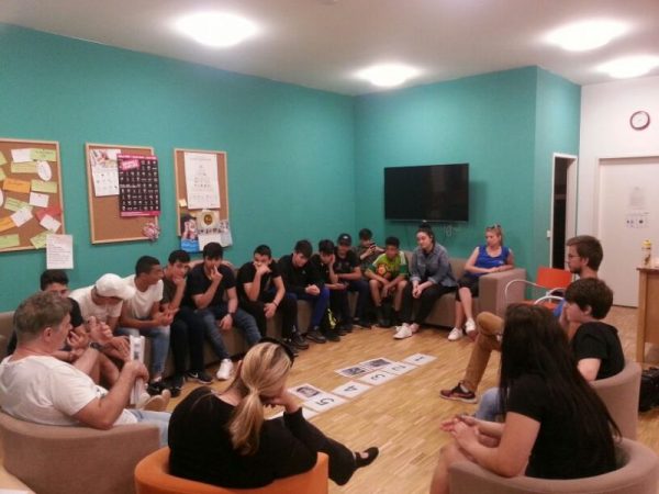 Viele junge Burschen sitzen in einem türkis bemalten Raum dicht gedrängt im Kreis. Auf dem Boden sind Ziffern geklebt und man erkennt, dass sie gerade intensiv an einem Workshop-Angebot teilnehmen.