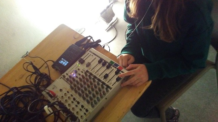 Ein Mädchen sitzt an einem Tisch, auf dem ein Mischpult steht, es hält die Finger auf einen Regler.
