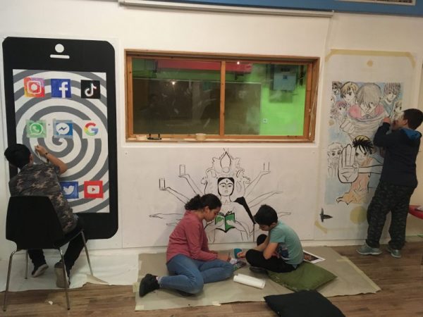 Vier Jugendliche malen und zeichnen an lebensgroßen Bildern für das im Artikel beschriebene Projekt. Verschiedene Handydisplays werden dargestellt.